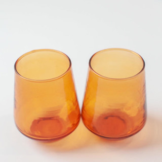 This is a orange tableware by Powered By People called handblown hammered glass water tumbler - amber - set of 4 in standard