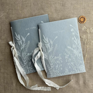 This is a blue vow books by Ivory Invitations called white ink print vellum covered english botanical garden blue vow books | set of 2 books | includes 1 her vows and 1 his vows in standard