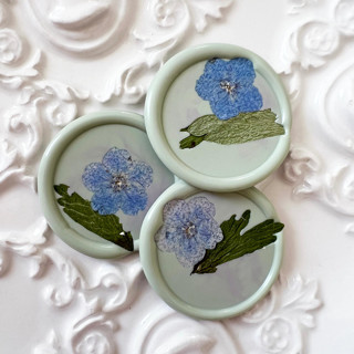 This is a green wax seals by Caitlin Home called blue forget me nots wax seal in celadon | pack of 10 in standard